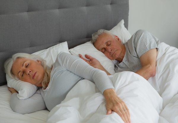 Front view of active senior Caucasian couple sleeping together in bed in bedroom at home