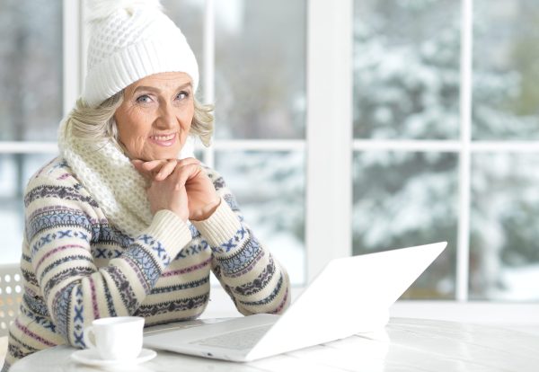 Mujer mayor utilizando un ordenador portátil, sentada cerca de una ventana